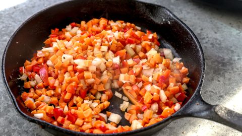 Onion, red bell pepper, and carrots sauteing in skillet.