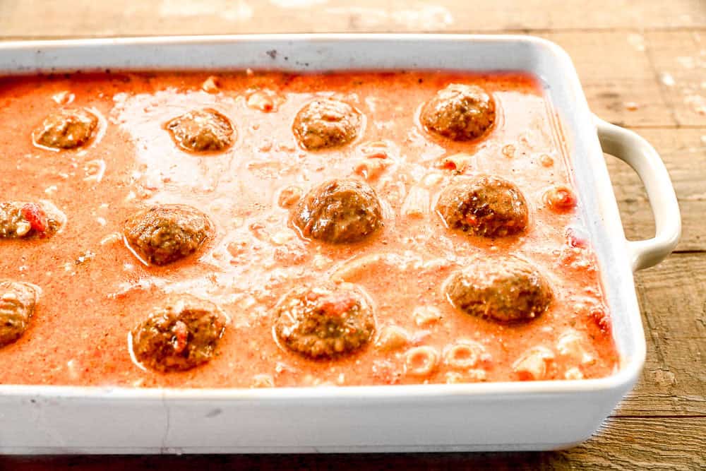 A white baking dish filled with meatballs in a creamy tomato sauce on a wooden surface.