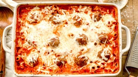 A casserole dish with baked meatball casserole, meatballs, and melted cheese on top, sitting on a wooden table.