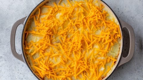 Round baking dish with sloppy joe casserole topped with a layer of shredded cheddar cheese.