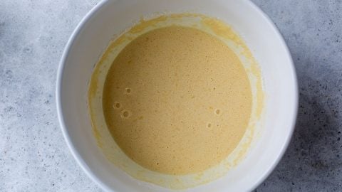 A white bowl filled with a light yellow, smooth Swedish pancake batter on a gray textured surface.