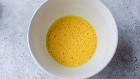 A white bowl with beaten eggs and bubbles on a gray speckled countertop.