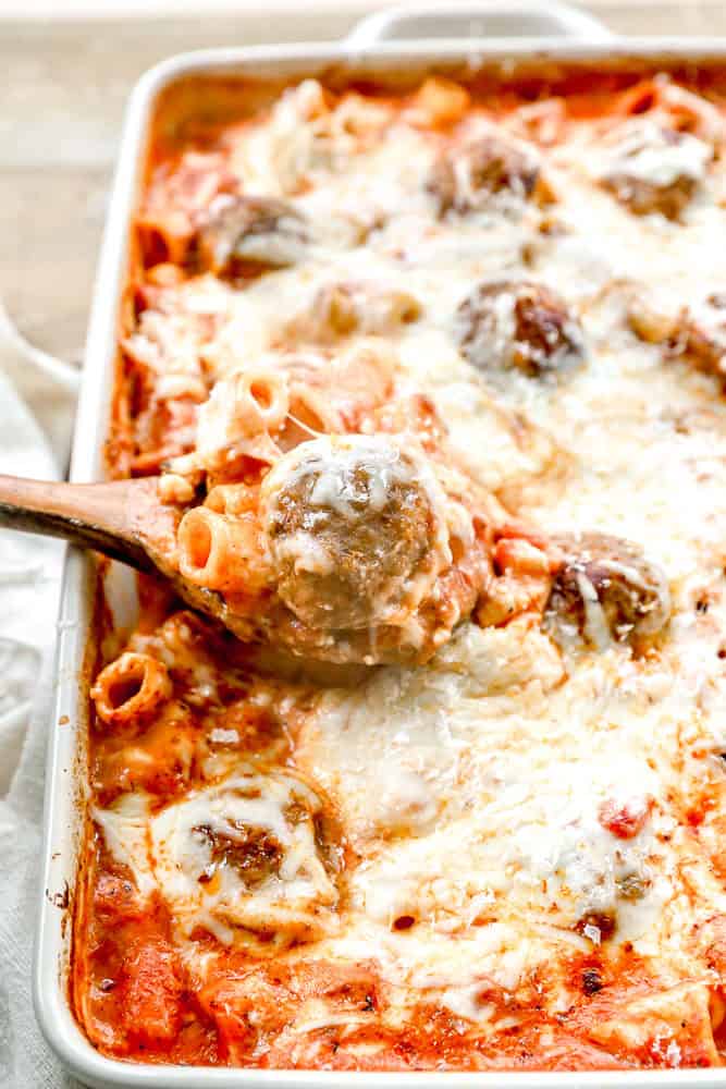 A baked meatball casserole with meatballs, marinara sauce, and melted cheese, being served with a wooden spoon.