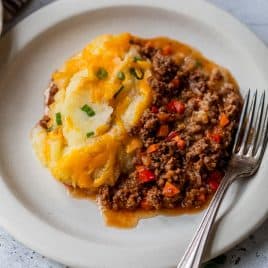 Sloppy joe casserole with ground meat, vegetables, and mashed potatoes topped with melted cheese on a plate with a fork.