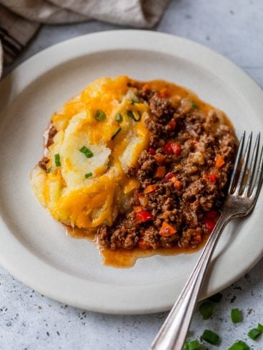 Sloppy joe casserole with ground meat, vegetables, and mashed potatoes topped with melted cheese on a plate with a fork.