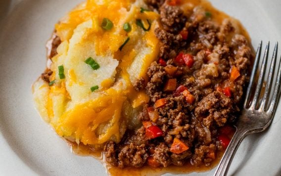Sloppy joe casserole with ground meat, vegetables, and mashed potatoes topped with melted cheese on a plate with a fork.