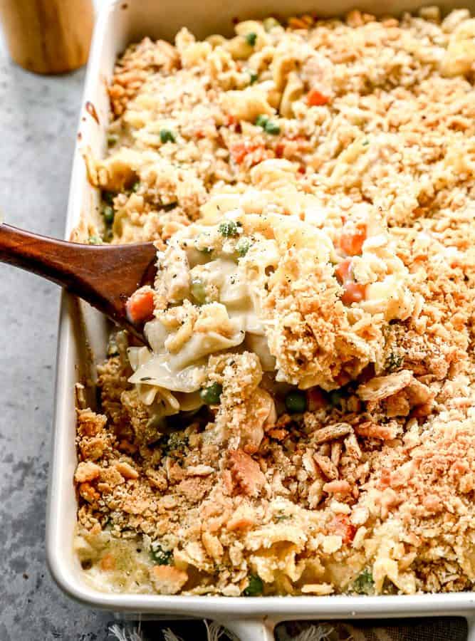 Wooden spoon scooping chicken noodle casserole from baking dish.