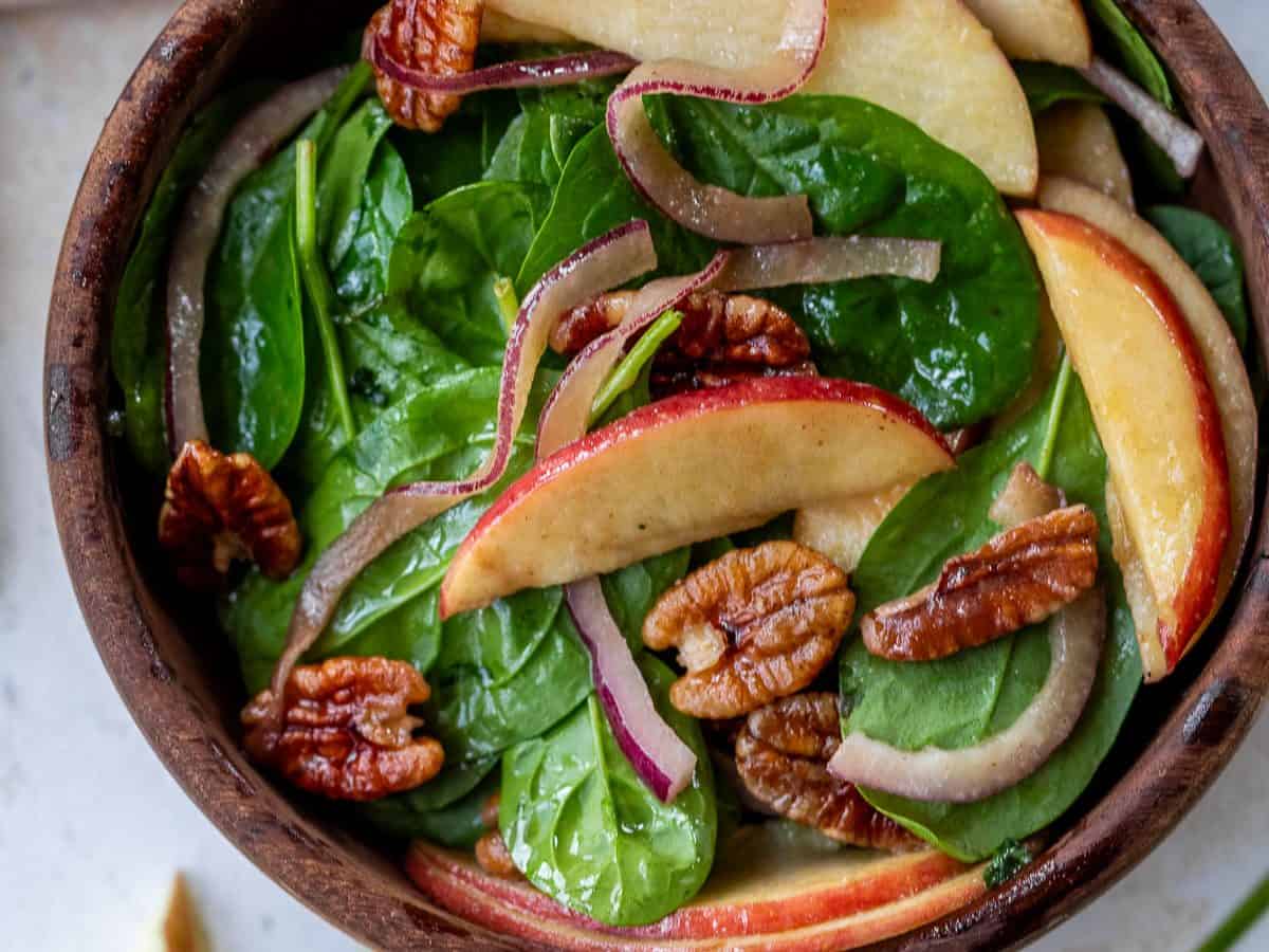 Spinach salad with apple, pecans, and onion in bowl.