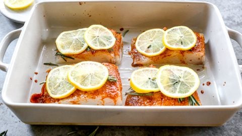 Uncooked halibut in baking dish with slices of lemon on top.
