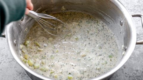 Whisking milk into pot of sauce.
