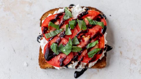 Slice of toast topped with cottage cheese, basil, sliced tomatoes, and balsamic glaze.