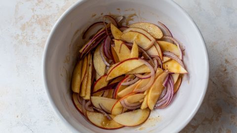 Sliced apples and red onion in bowl.
