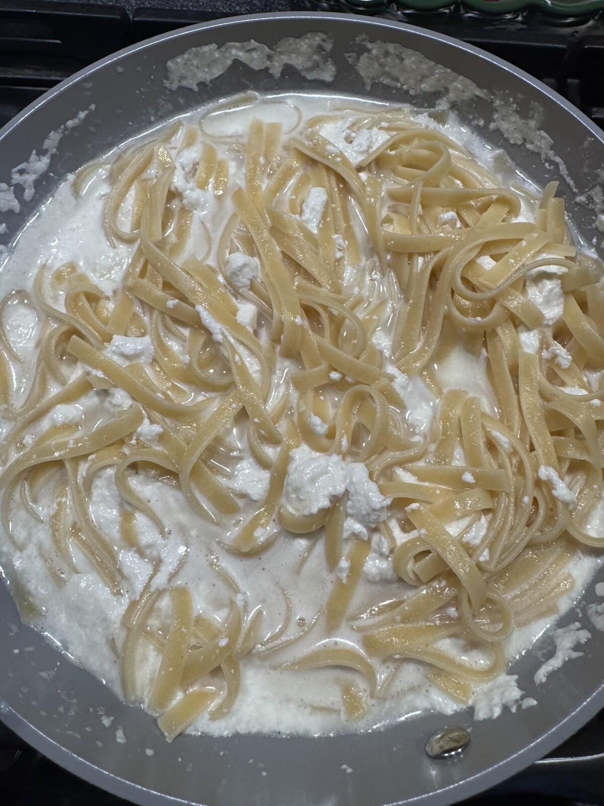 Fettuccine pasta in a creamy white sauce cooking in a large pan on the stove.