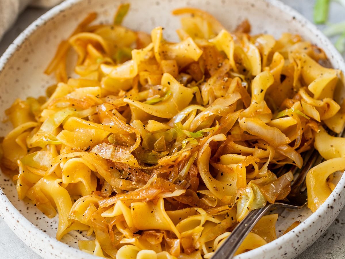 A bowl of cabbage and noodles, with a fork resting on the plate.