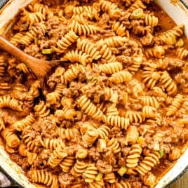 Cheeseburger casserole in a creamy tomato sauce, mixed in a large pot with a wooden spoon.