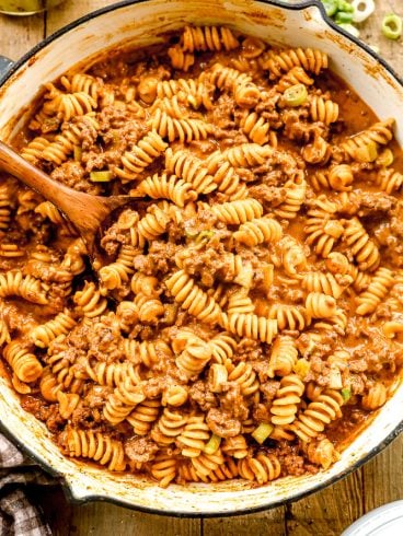 Cheeseburger casserole in a creamy tomato sauce, mixed in a large pot with a wooden spoon.