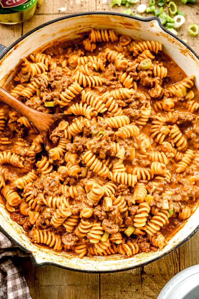 Cheeseburger casserole in a creamy tomato sauce, mixed in a large pot with a wooden spoon.