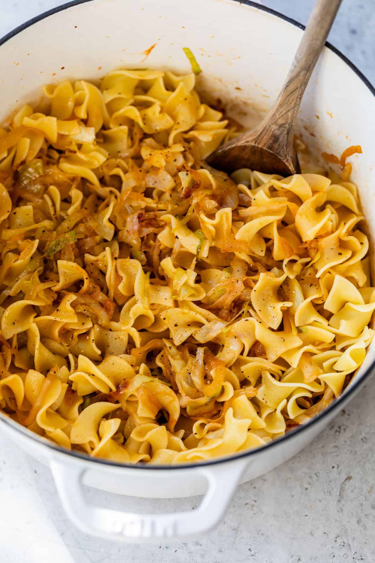 Wide white pot filled with cabbage and noodles, with a wooden spoon inside.