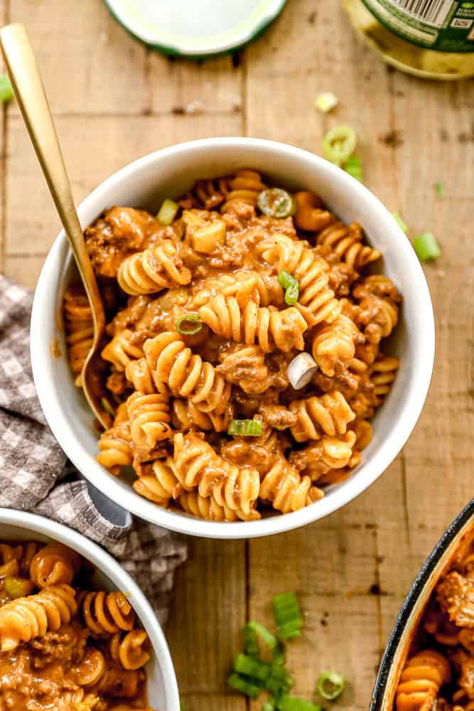 A bowl of cheeseburger casserole with creamy sauce, ground meat, and chopped green onions, served with a gold spoon.