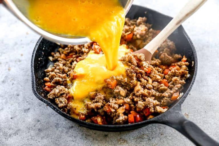 Pouring eggs into pan with sausage.