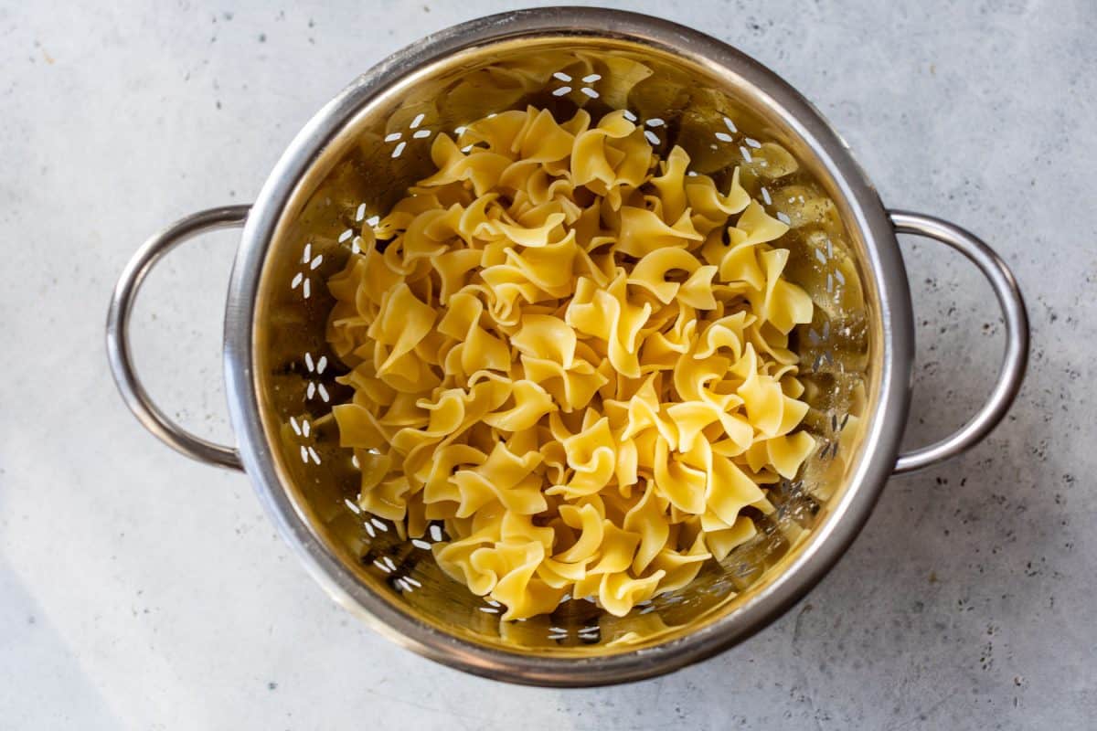 Cooked egg noodles in a metal colander, draining on a light-colored countertop.