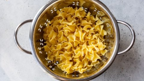 Cooked egg noodles in a metal colander, draining on a light-colored countertop.