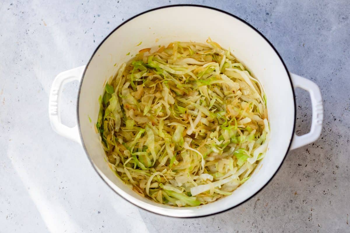 Sautéed shredded cabbage in a white pot on a light gray surface.
