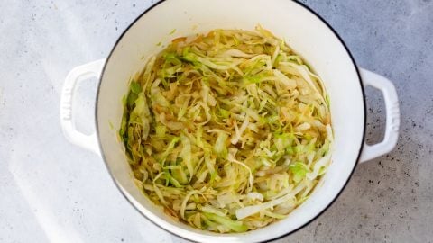 Sautรฉed shredded cabbage in a white pot on a light gray surface.