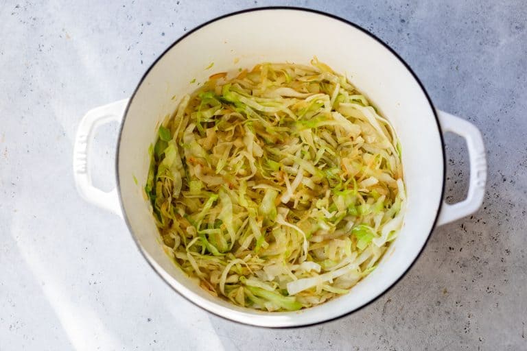 Sautéed shredded cabbage in a white pot on a light gray surface.