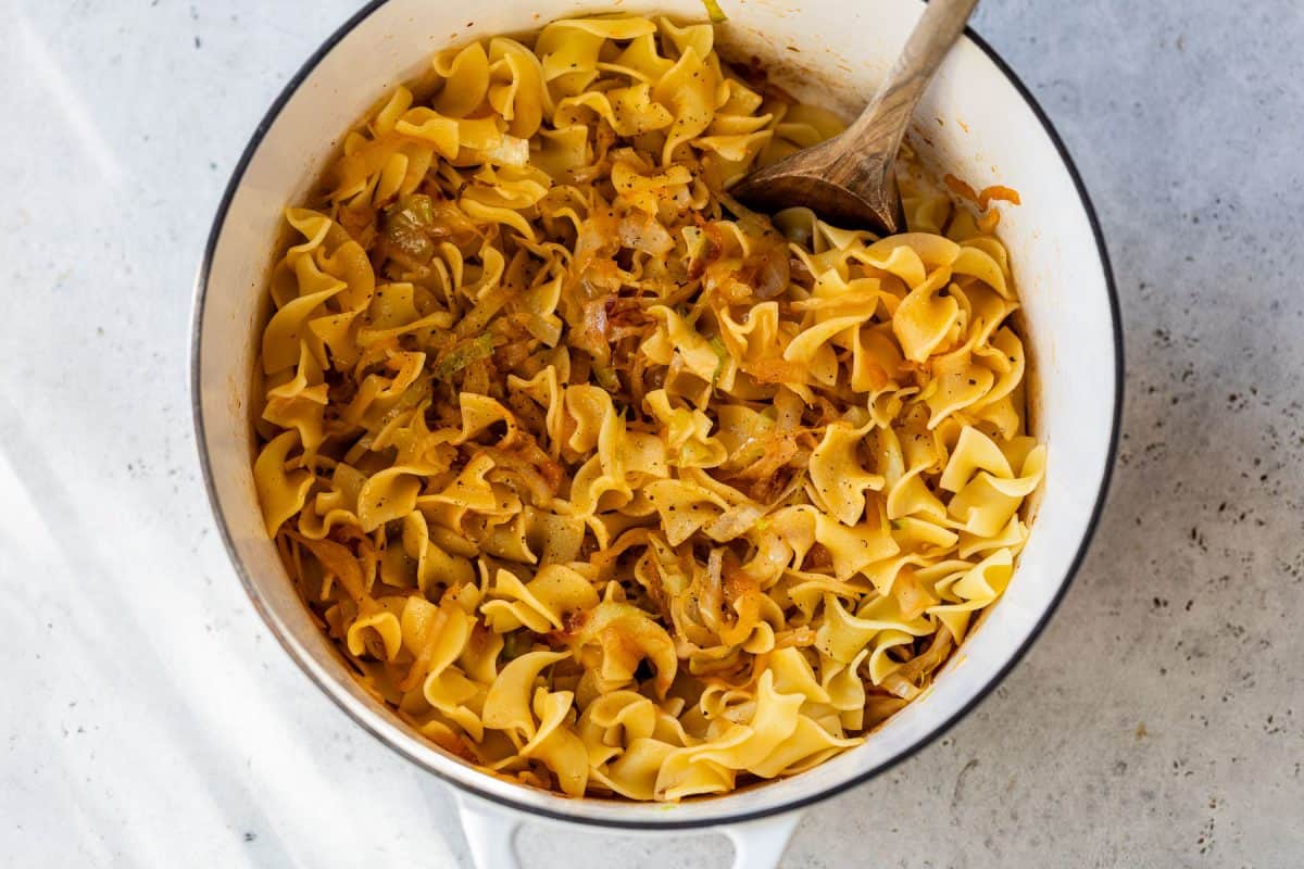 A pot of cabbage and noodles, stirred with a wooden spoon.