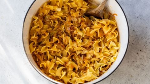 A pot of cabbage and noodles, stirred with a wooden spoon.