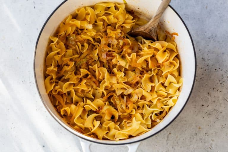 A pot of cabbage and noodles, stirred with a wooden spoon.