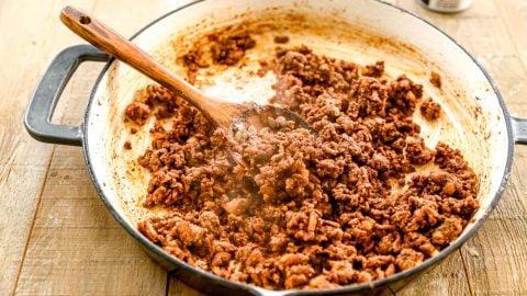 Cooked seasoned ground beef in a skillet with a wooden spoon on a wooden table.