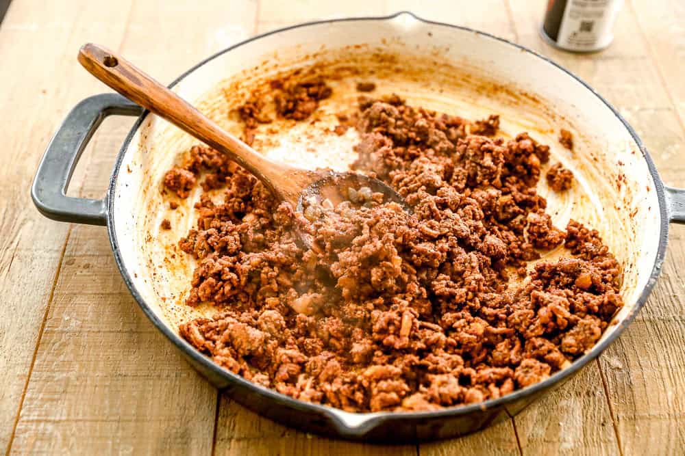 Cooked seasoned ground beef in a skillet with a wooden spoon on a wooden table.