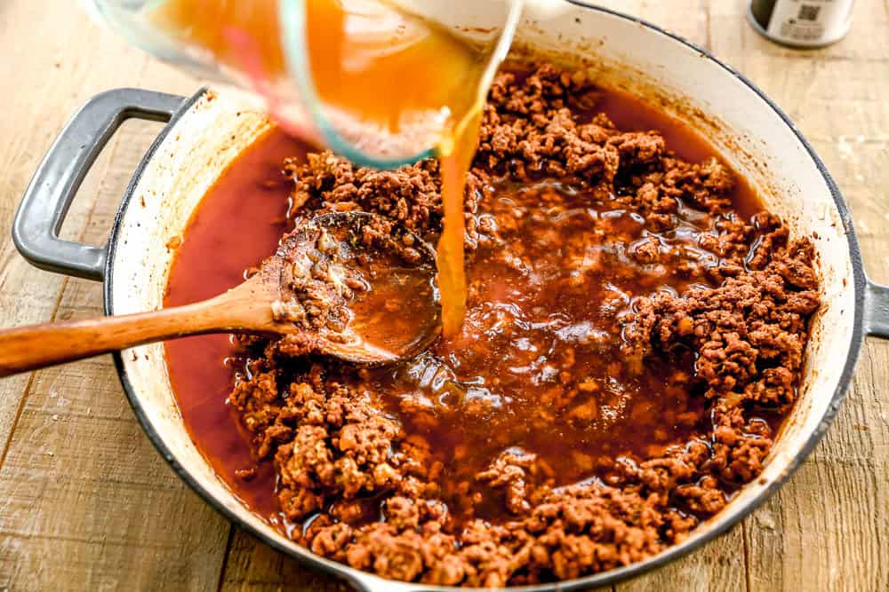 Ground beef simmering in a pan as broth is poured in, with a wooden spoon stirring the mixture.