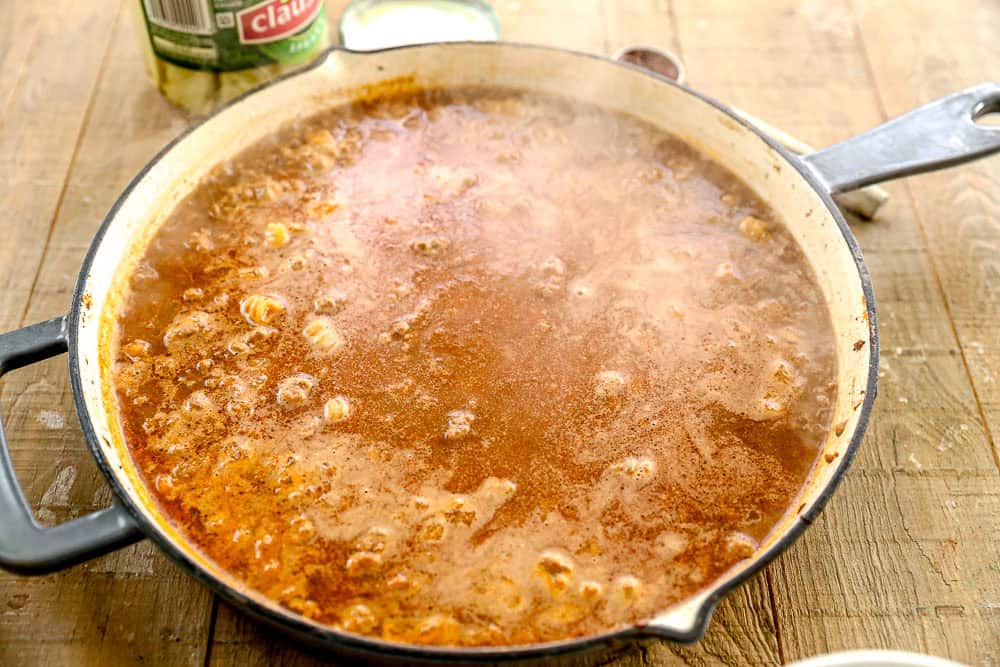 A large skillet on a wooden table filled with simmering, reddish-brown broth.
