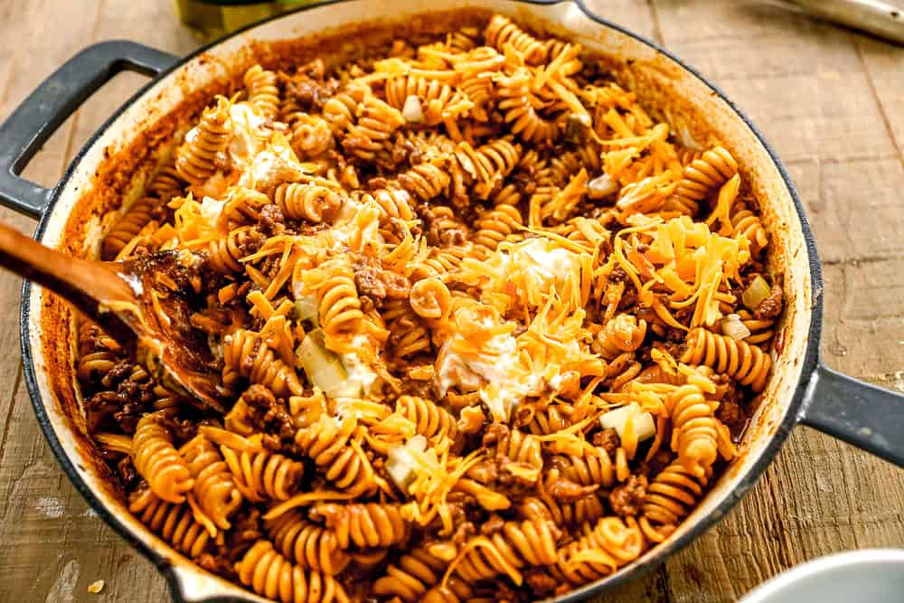 A skillet filled with cheeseburger casserole being stirred with a wooden spoon.