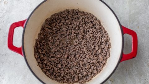 Cooked ground beef in a large red Dutch oven on a light-colored countertop.