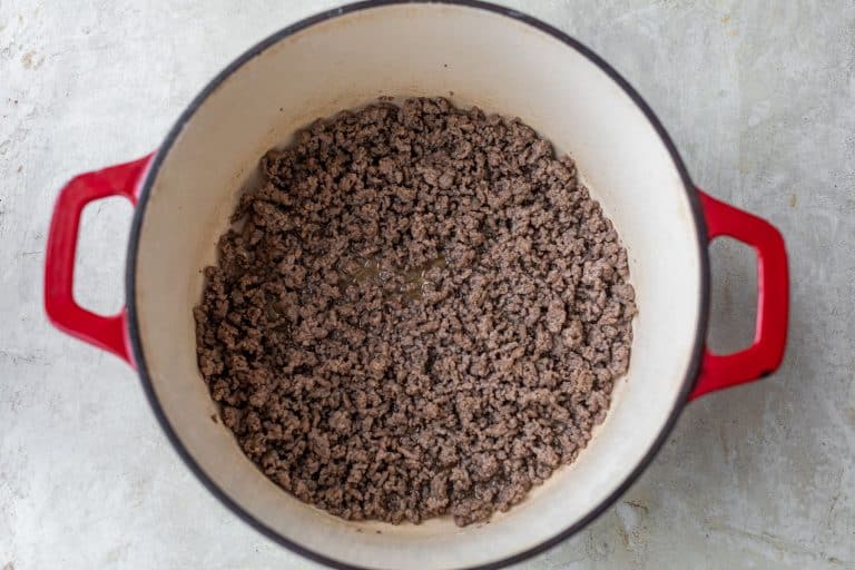 Cooked ground beef in a large red Dutch oven on a light-colored countertop.