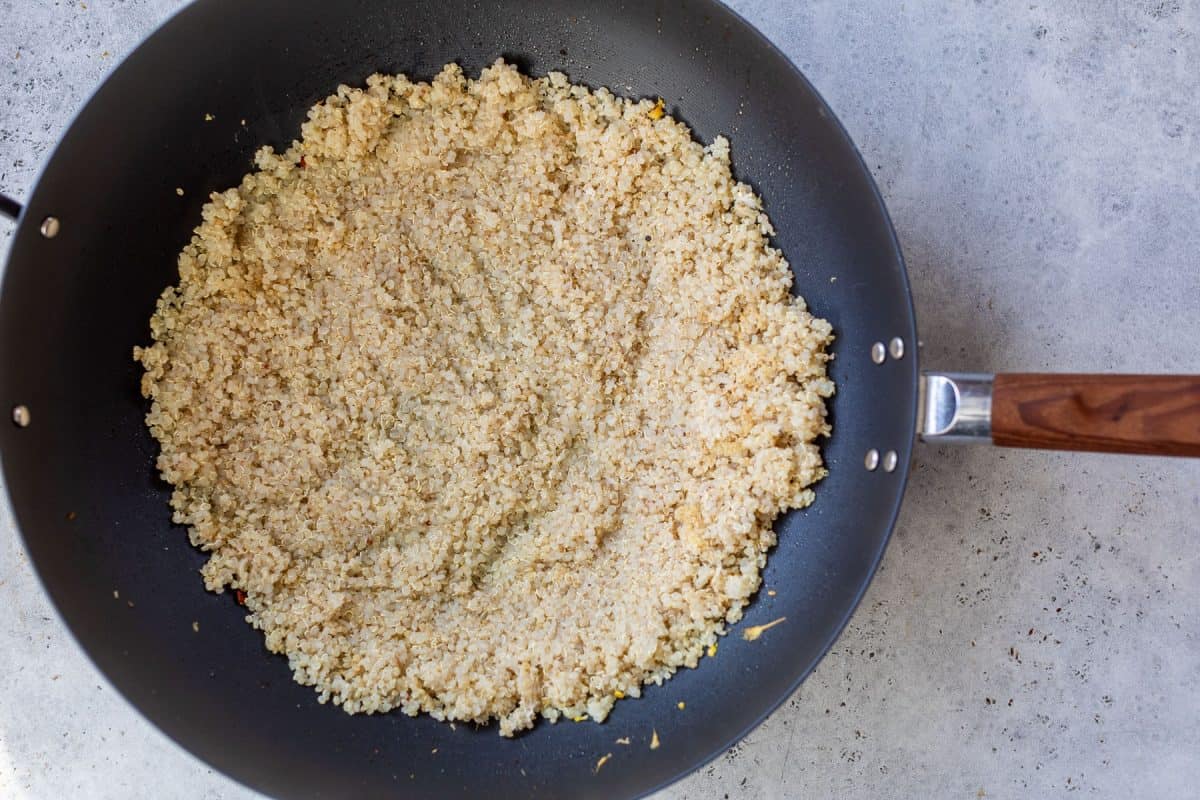 Cooked quinoa in a black frying pan with a wooden handle, resting on a light gray countertop.