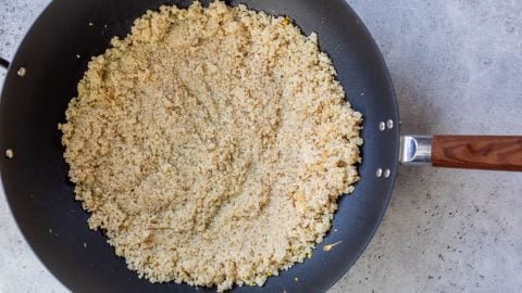 Cooked quinoa in a black frying pan with a wooden handle, resting on a light gray countertop.