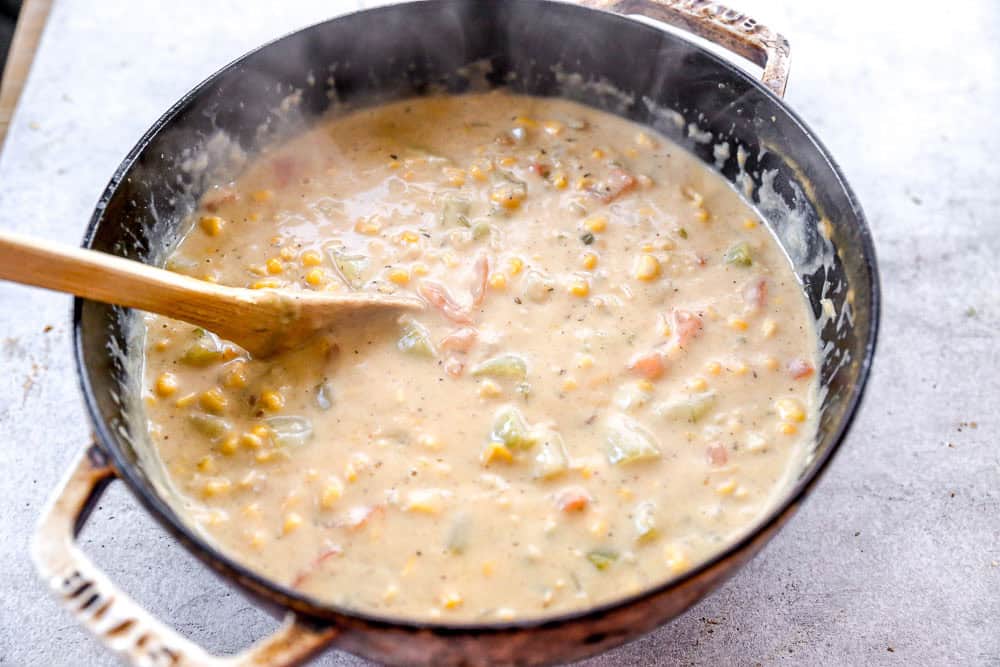 A pot of creamy salmon chowder with vegetables being stirred by a wooden spoon.