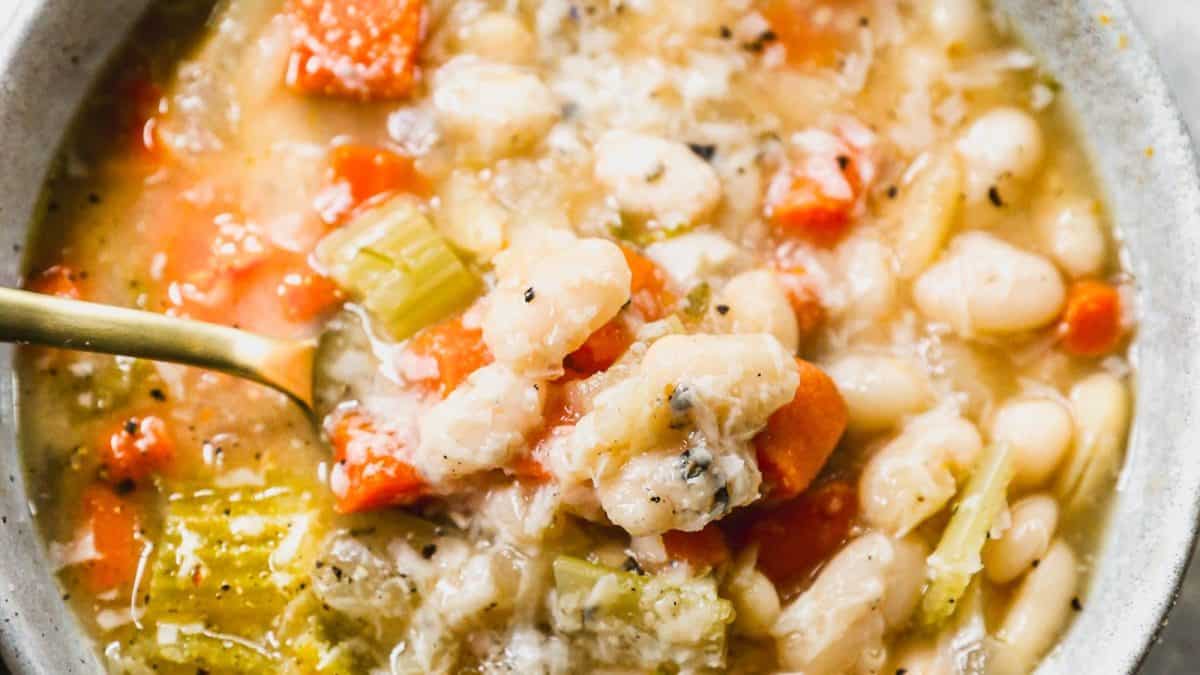A close-up of a bowl of vegetable and bean soup with carrots, celery, and white beans in a broth.