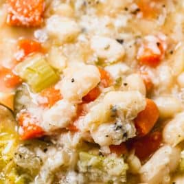 A close-up of a bowl of vegetable and bean soup with carrots, celery, and white beans in a broth.
