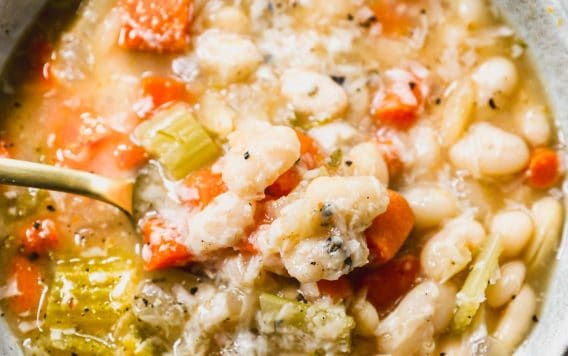 A close-up of a bowl of vegetable and bean soup with carrots, celery, and white beans in a broth.