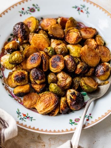 A plate of caramelized Brussels sprouts with a spoon, on a decorative white dish with floral patterns.