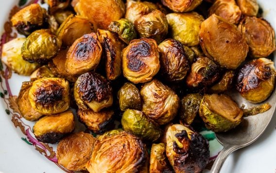 A plate of caramelized Brussels sprouts with a spoon, on a decorative white dish with floral patterns.