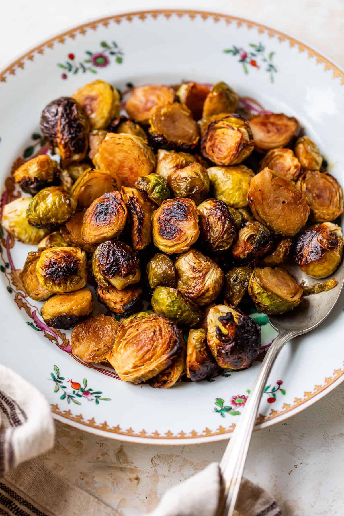 A plate of caramelized Brussels sprouts with a spoon, on a decorative white dish with floral patterns.