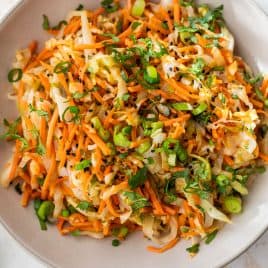 A bowl of sauteed cabbage and carrots with green onions, cilantro, and black sesame seeds.