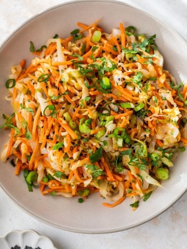 A bowl of sauteed cabbage and carrots with green onions, cilantro, and black sesame seeds.